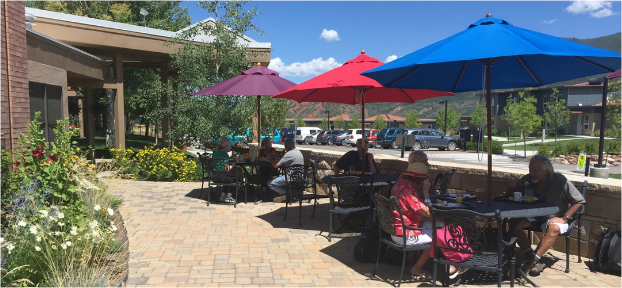 the patio of the senior center with people seated at tables and chairs with colorful shade umbrellas