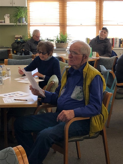 a man and woman sit at a table looking at papers during a presentation at the senior center